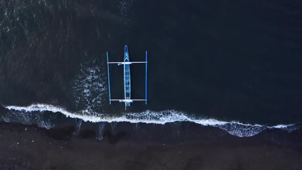 Aerial Top View of a Blue Fishing Boat Floating on Sea Water with Waves Rolling on Beach alt