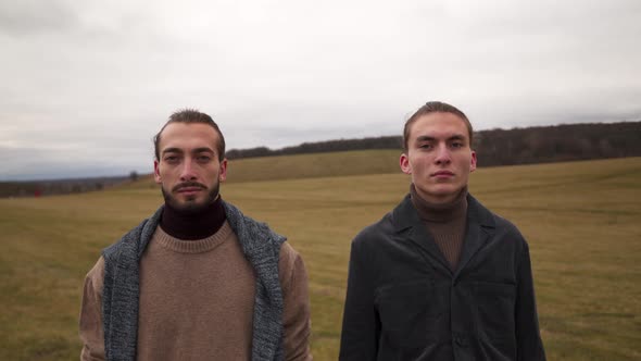 Two Men in Lights Stand in Field in Cloudy Autumn Weather Looking at the Camera