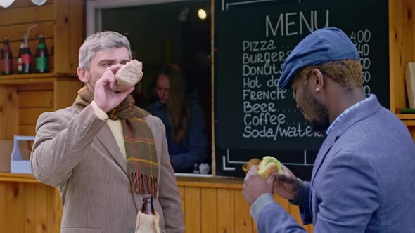 Two men drinking and eating near food booth