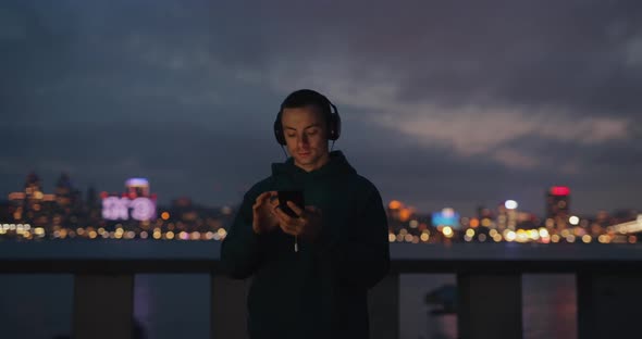 Man Using Phone in Headphones in Evening City alt