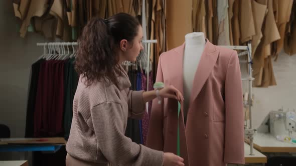 seamstress is measuring clothing suit to tailoring dummy with measure-tape. alt