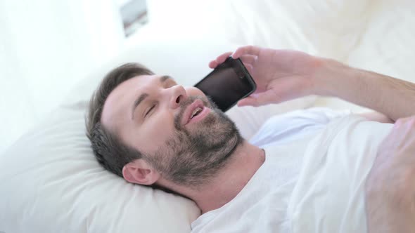 Cheerful Beard Young Man Designer Talking on Smartphone in Bed alt
