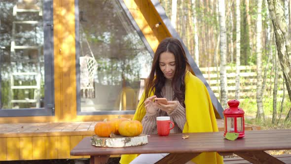 Happy Young Woman Drinking Coffee Sitting at the Wooden Table Outdoors