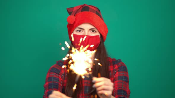 Pretty Woman with Firework Sparkler and Christmas Hat While Wearing Protective Face Mask for