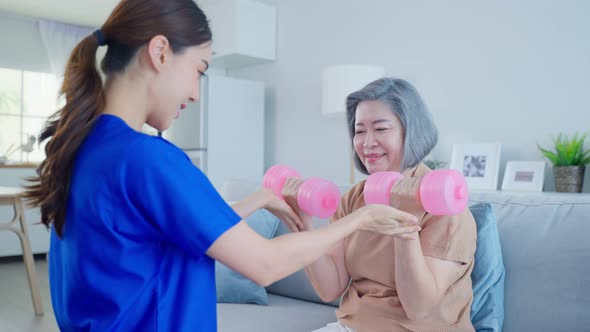 Asian Disabled older woman using dumbbells workout doing physiotherapist with support from nurse. alt