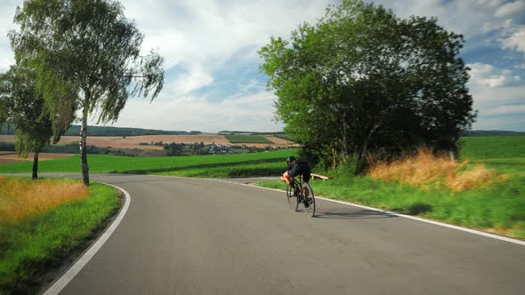 Cyclist riding bicycle down mountain road in sunshine.  alt