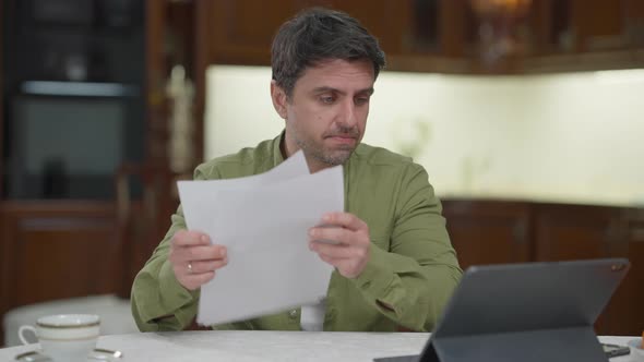 Unshaved Confident Professional Caucasian Man Analyzing Paperwork and Emarket on Remote Working at alt