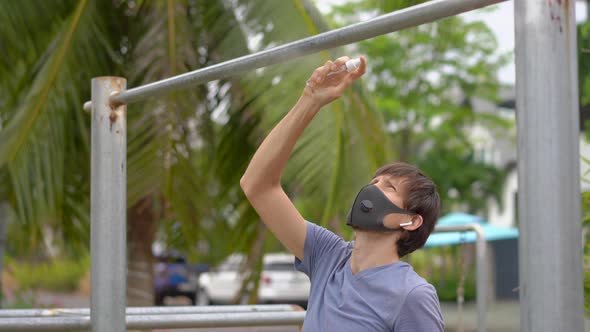 A Young Man Disinfects Pull-up Bar on a Street. Then He Starts Doing Exercises. Physical Exercises alt