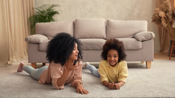 African American Woman and Litle Girl Watching TV Switching Channels with Remote Control alt
