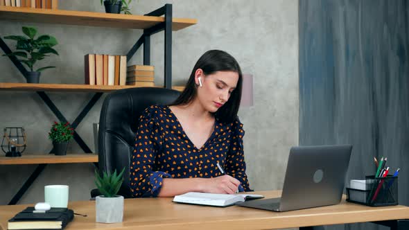 Woman student in home office writes in notebook study remote online chat webcam laptop computer alt