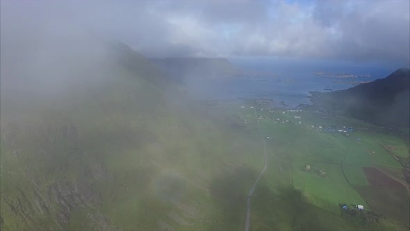 Flying in the clouds above green farmland on Lofoten alt