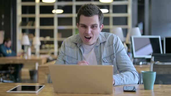 Surprised Young Designer Celebrating Success on Laptop in Office alt