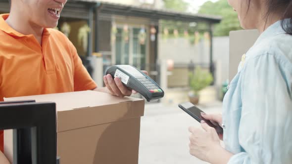 Asian women signing and pay via qr code on mobile phone for receive delivered parcels outdoors. . alt