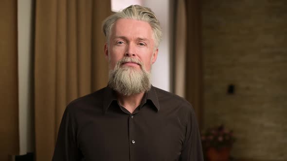 stylish adult bearded gray-haired man calmly looks straight into the camera alt