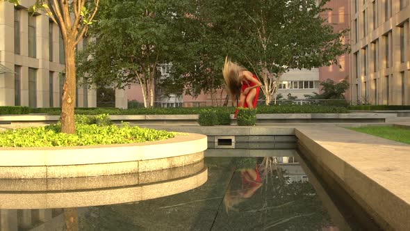 Beautiful Young Girl Dancing on the Street of a Modern City and Is Reflected in the Water alt