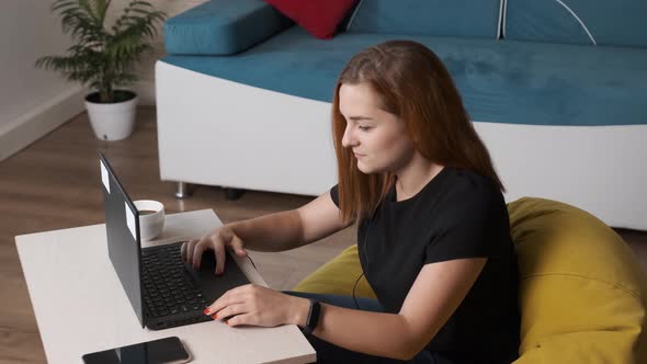 Young Woman Is Drinking a Cup of Coffee While Is Working at the Laptop From Home Office. alt
