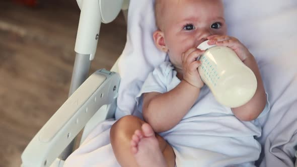 Cute Little Newborn Girl Drinking Milk From Bottle and Looking at Camera on White Background alt