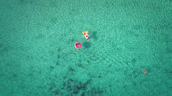 Close aerial view of two young girls swimming and playing in sea with inflatables.