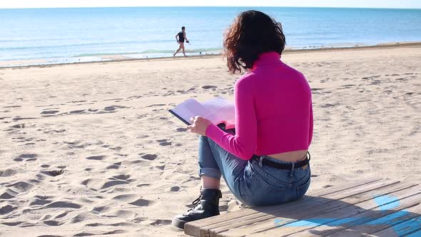 Dressed Girl Reading a Book Sitting on the Sand