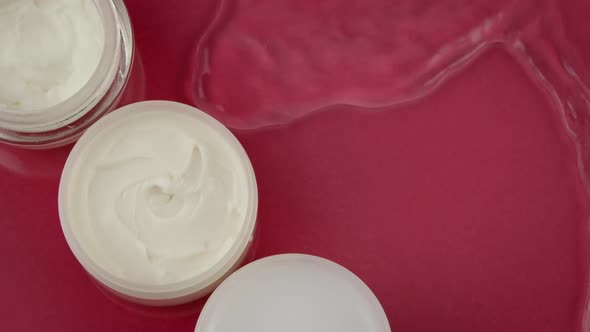 Cosmetic Jars with Moisturizing Cream in Clean Water Splash on Red Background