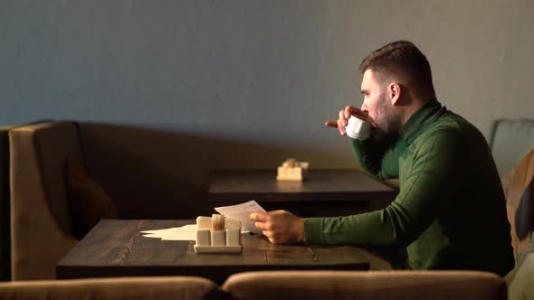 a Bearded Businessman Sits in a Cafe and Checks the Contract