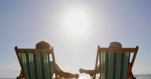 Couple relaxing on sun lounger at beach in the sunshine 4k