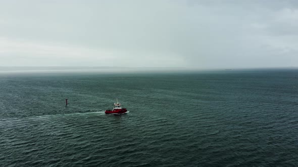 Drone Shot Tug Boat Goes to the Open Sea in Stormy Weather Behind a Cargo Ship alt