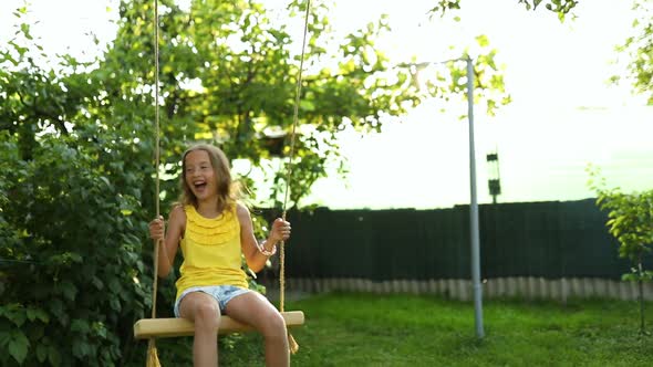 Happy barefoot laughing child girl swinging on a swing in sunset summer day