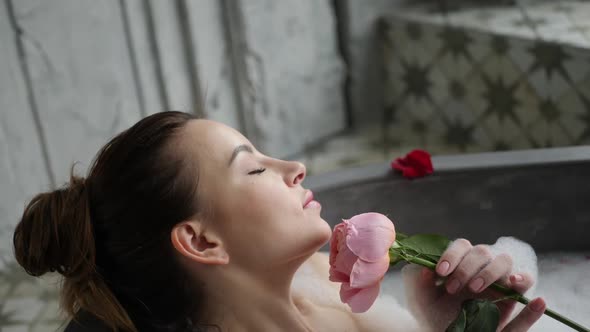 Sexy Girl Lies in a Big Stone Bath with a Rose Flower in Her Hands alt