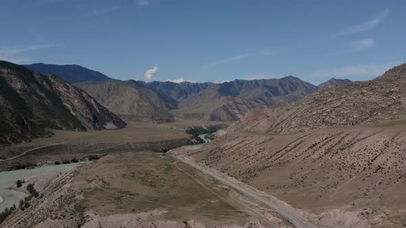 Traffic cars on road between mountains of Altai under clear blue sky