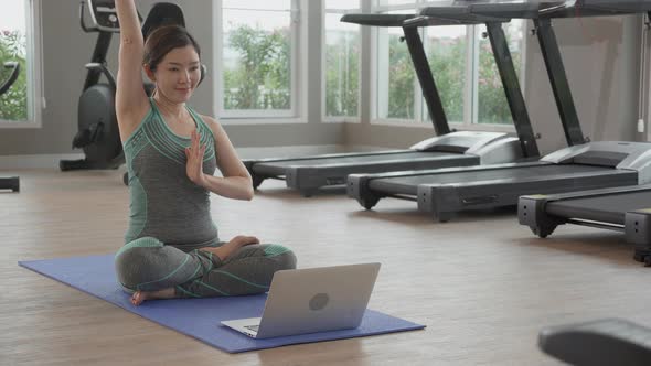 Young asian woman doing yoga with sitting and stretch muscles hands at fitness gym. alt