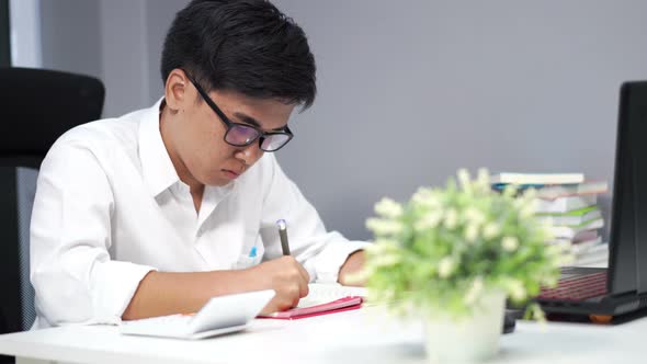 young man studying and writing on notebook with laptop computer alt