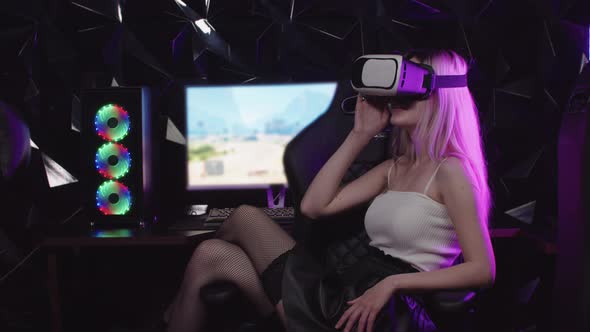 Young Blonde Gamer Girl Sitting in a Chair Wearing VR Glasses alt