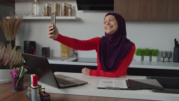 Joyful Attractive Middle Eastern Female in Hijab Posing for Selfie Shot on Cellphone Indoors alt