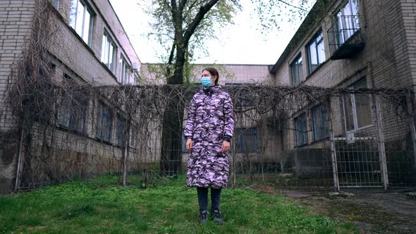 The Woman in Mask Outside During the Pandemic. Health Care and Medical Concept. Abandoned Facility