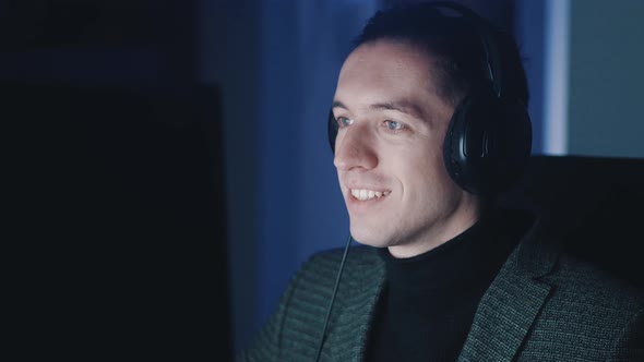Smiling Businessman Man in Headphones Listening Music and Working at Computer Late at Night