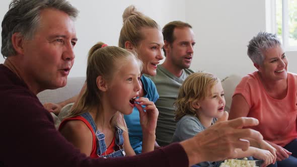 Excited caucasian three generation family sitting on couch watching tv and cheering alt