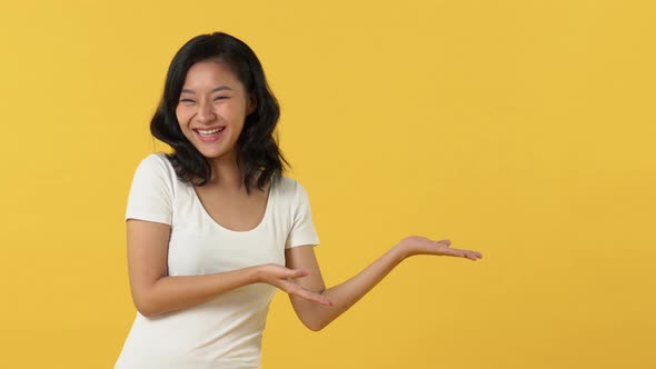 Happy smiling young Asian woman open hands and pointing to empty space