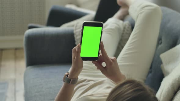 Female on Sofa Watching Green Smartphone Screen