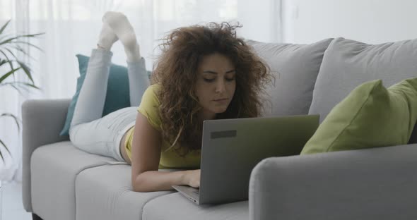 Woman lying on the sofa and using her laptop