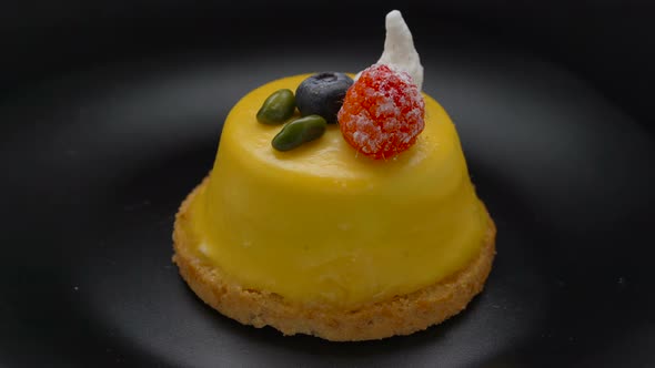 Mango mousse cake covered with yellow glaze rotating on black plate