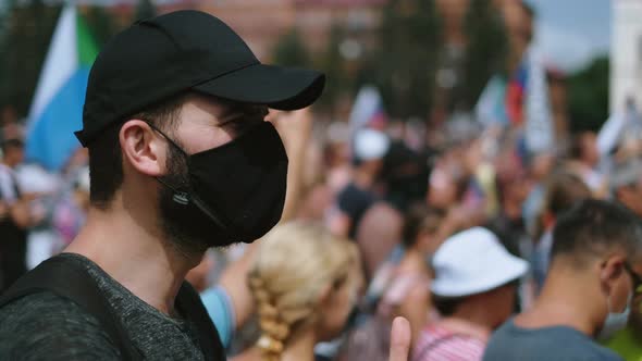 Applauding Male Activist in Mask and Cap Stands Among Opposition People Riot alt