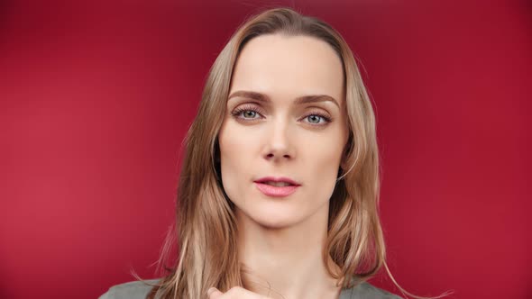 Face of Beautiful Young Blonde Woman Showing Silence Gesture Posing at Red Studio Background alt