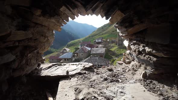 Dolly into a top old village view through an old stone tower half circle window, mountain background alt