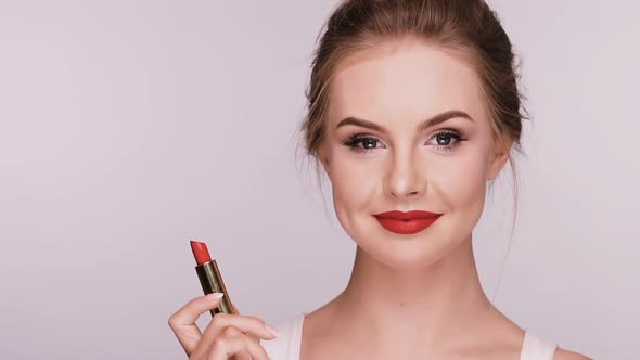 Attractive Woman Applies Red Lipstick and Smiles Isolated on Grey alt