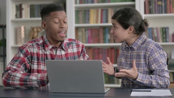 African Man and Indian Woman Arguing while Working on Laptop alt
