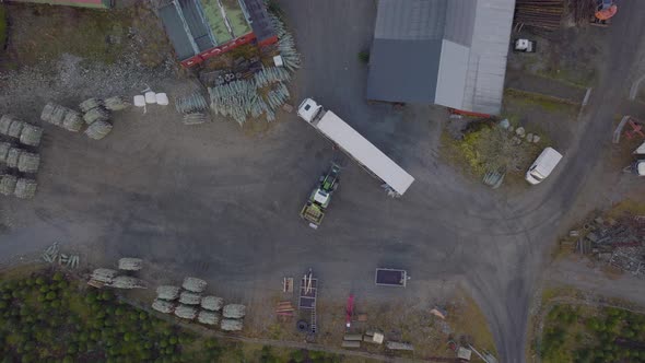 Tractor loads Christmas trees on white truck on farmyard; aerial riser alt
