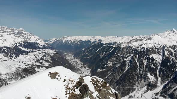 Flyover mountain top revealing the valley behind. Snow covered Swiss mountains in winter. alt