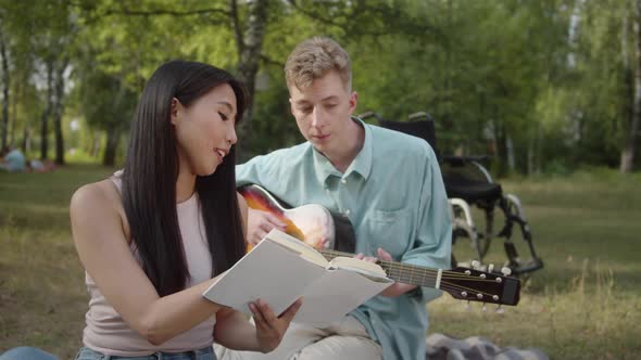 A Young Pretty Asian Girl is Sitting on the Plaid and Looking Through the Book While Her Disabled