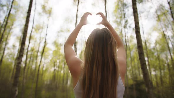 Young Caucasian Woman Framing Sun with Her Hands in Heart Shape. Copy Space alt